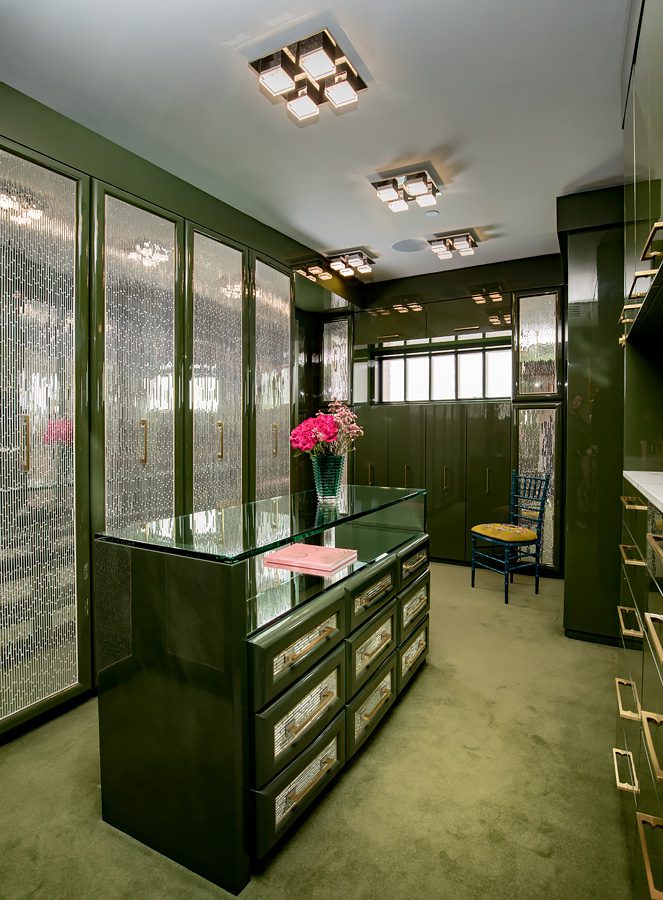 A walk in closet with green cabinets and a glass top.