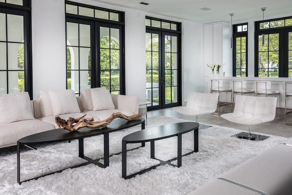 A white living room with large windows and black furniture.