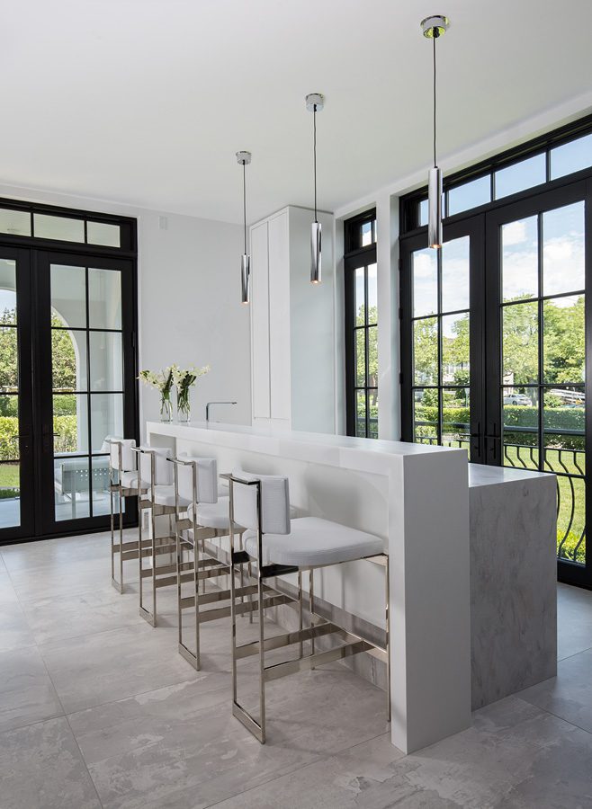 A modern kitchen with white counter tops and large windows.