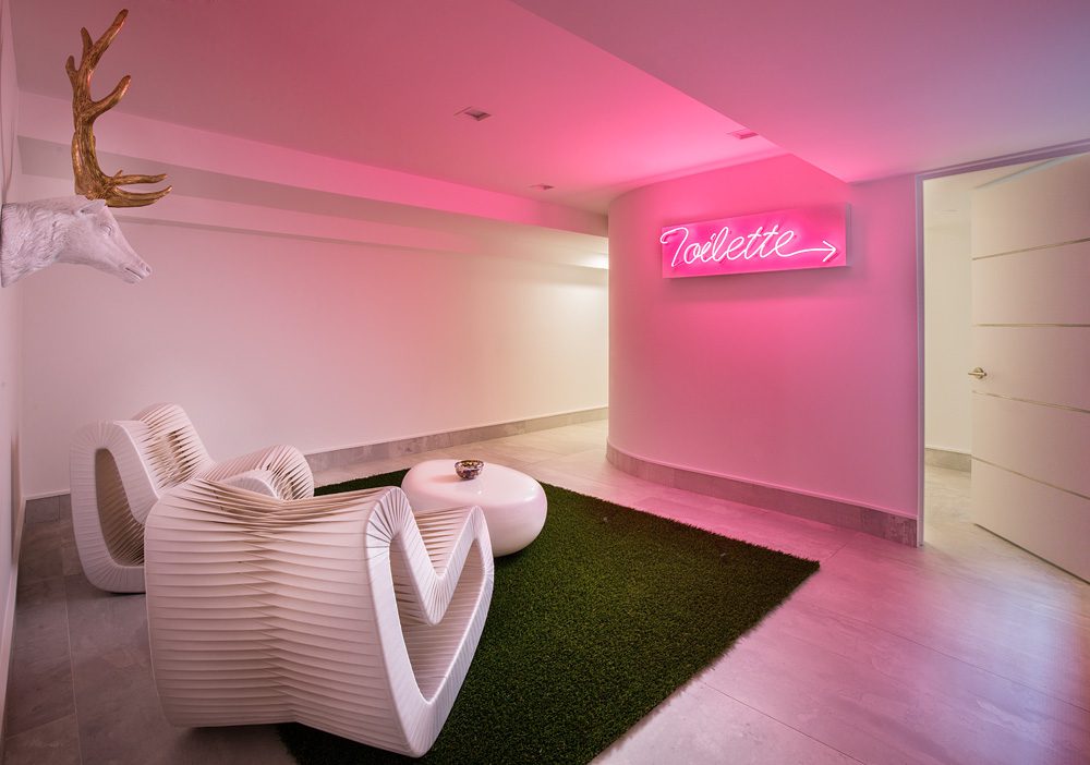 A room with a pink neon sign and a white chair.