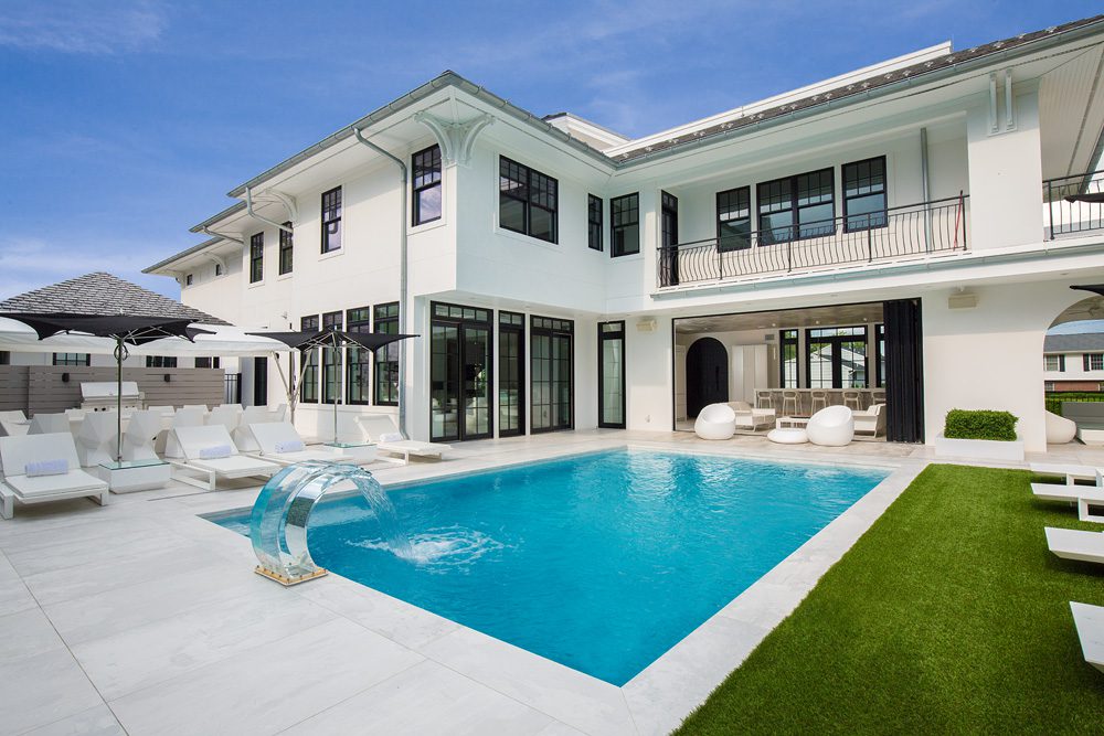 A white house with a pool and lounge chairs.