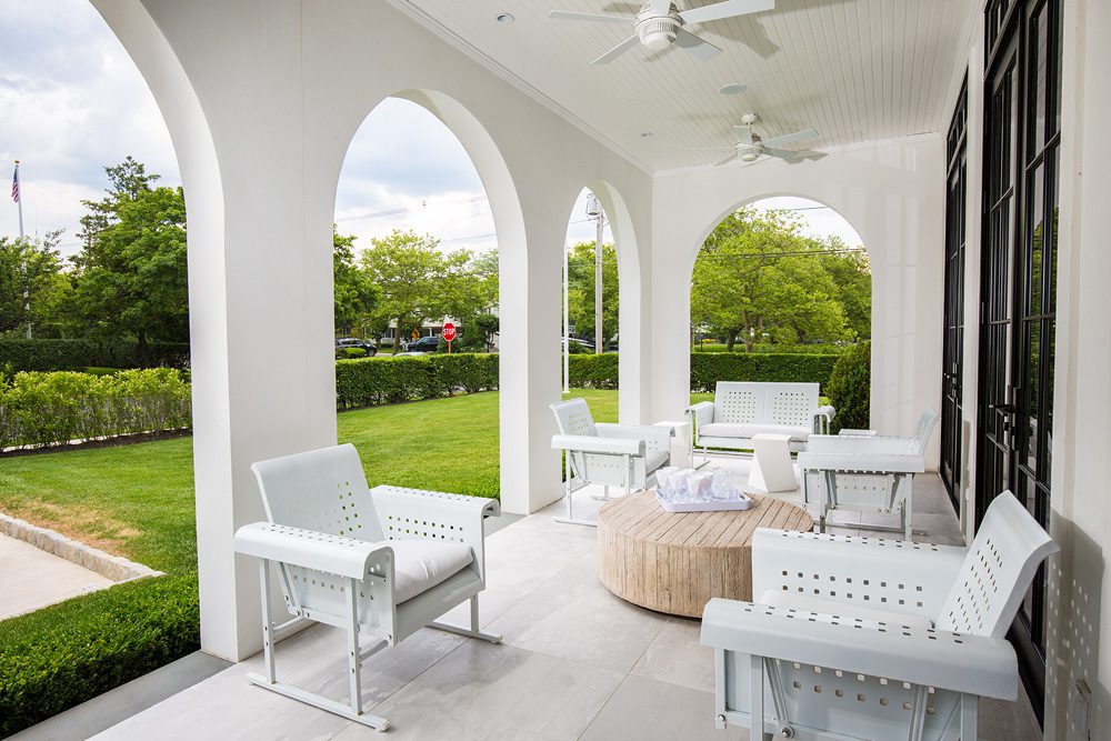 A porch with white chairs and a table.